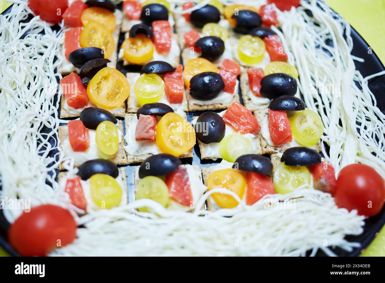 Dark dish with threads of sulguni and many tartines with pieces of olive, red fish and roma tomato. Stock Photo