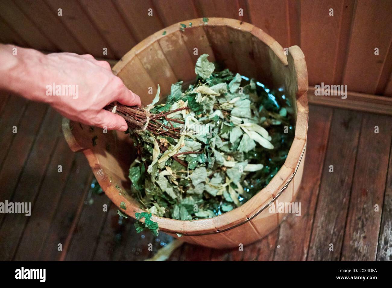 Male hand holds besom in wooden bucket in sauna. Stock Photo