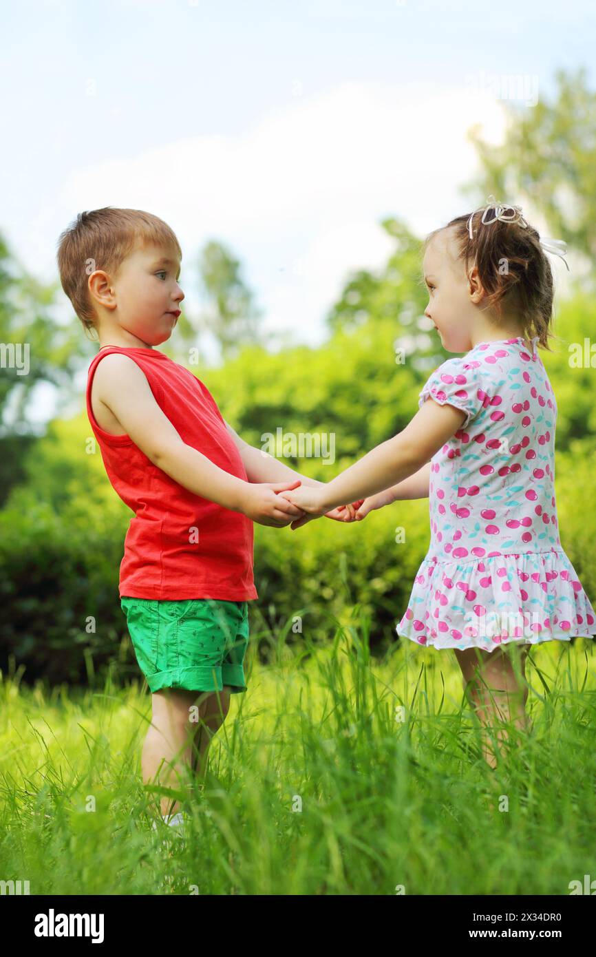 Little girl and boy hold hands on fresh green grass in park Stock Photo ...