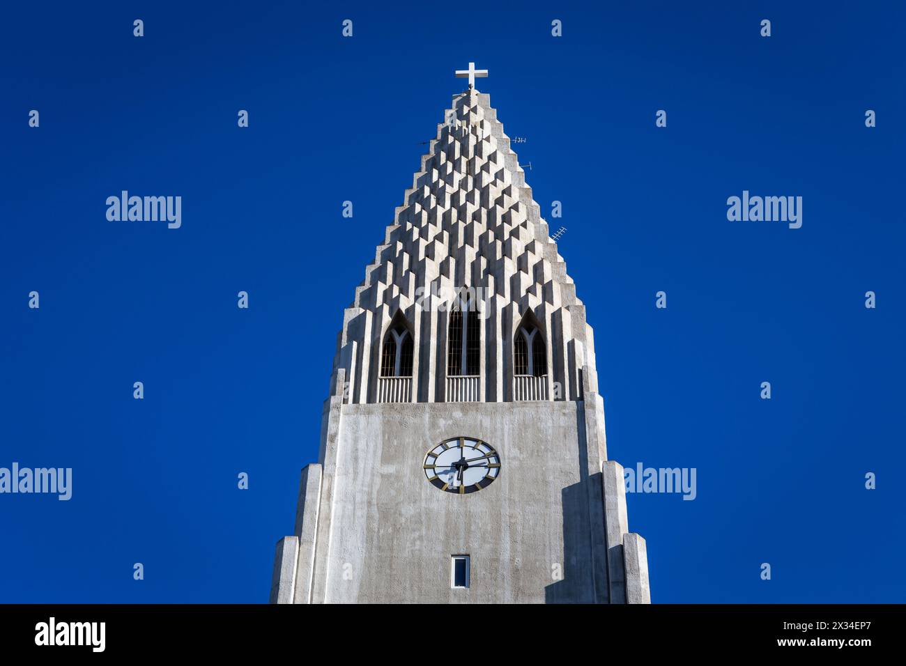 Hallgrimskirkja church tower top with Holy Cross and clock, Reykjavik, Iceland, modern belfry against clear blue sky, symmetrical view. Stock Photo