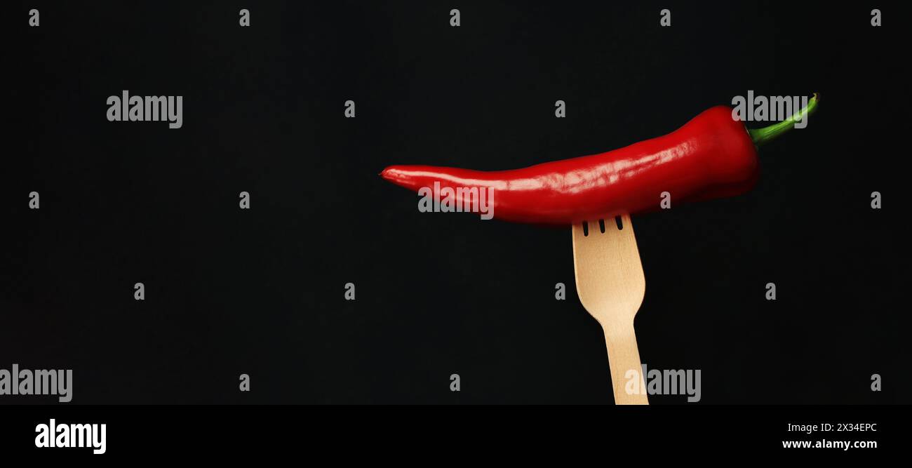 Red hot pepper on a wooden disposable fork, close-up, dark background. Pepper on a dark background. Concept of food, fresh vegetables and spices Stock Photo