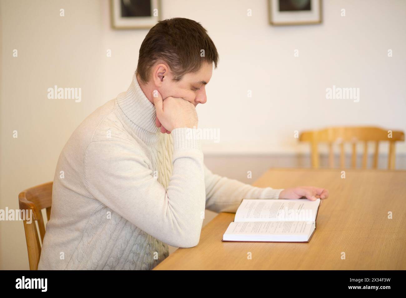 Man in white sits at table and reads book and thinks in empty room Stock Photo