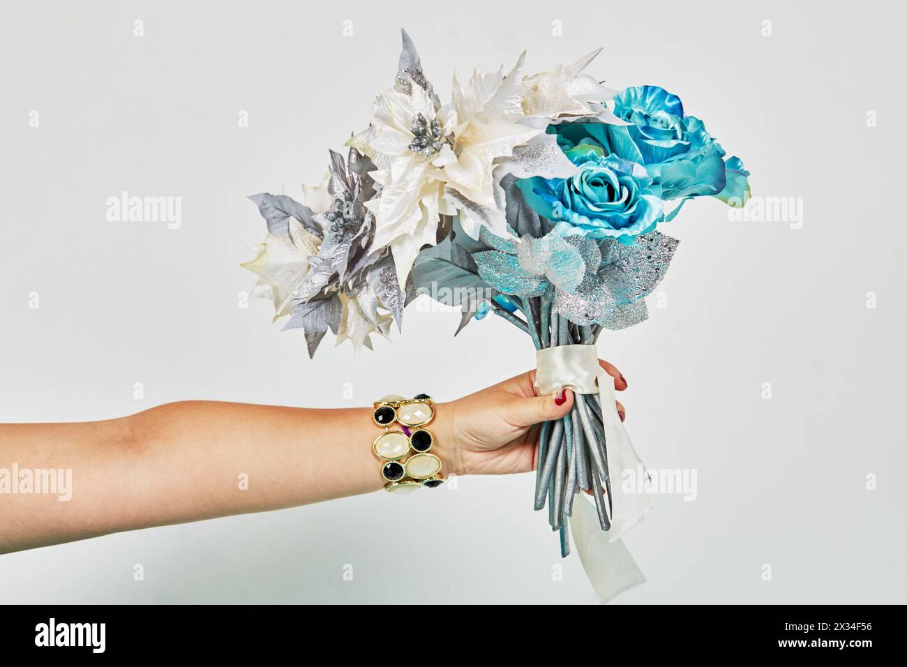 Outstretched female hand with bracelet holds bunch of artificial flowers. Stock Photo