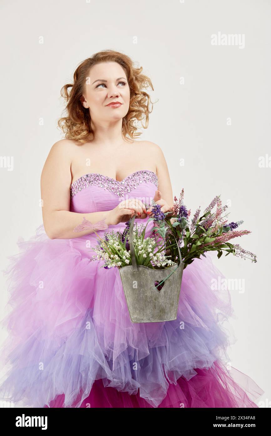 Portrait of smiling woman in a fluffy purple dress with bag full of flowers. Stock Photo