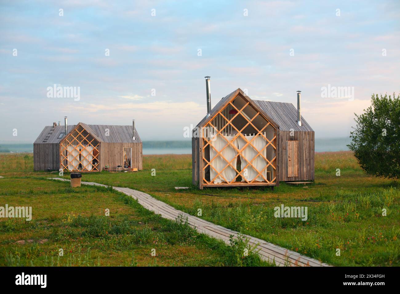Several small wooden hotel cottages in meadow in morning mist. Stock Photo