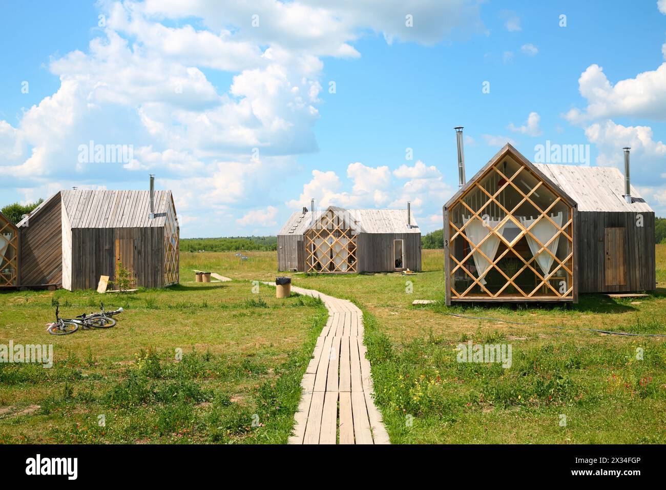 Several small guest wooden houses on meadow in forest sunny summer day. Stock Photo