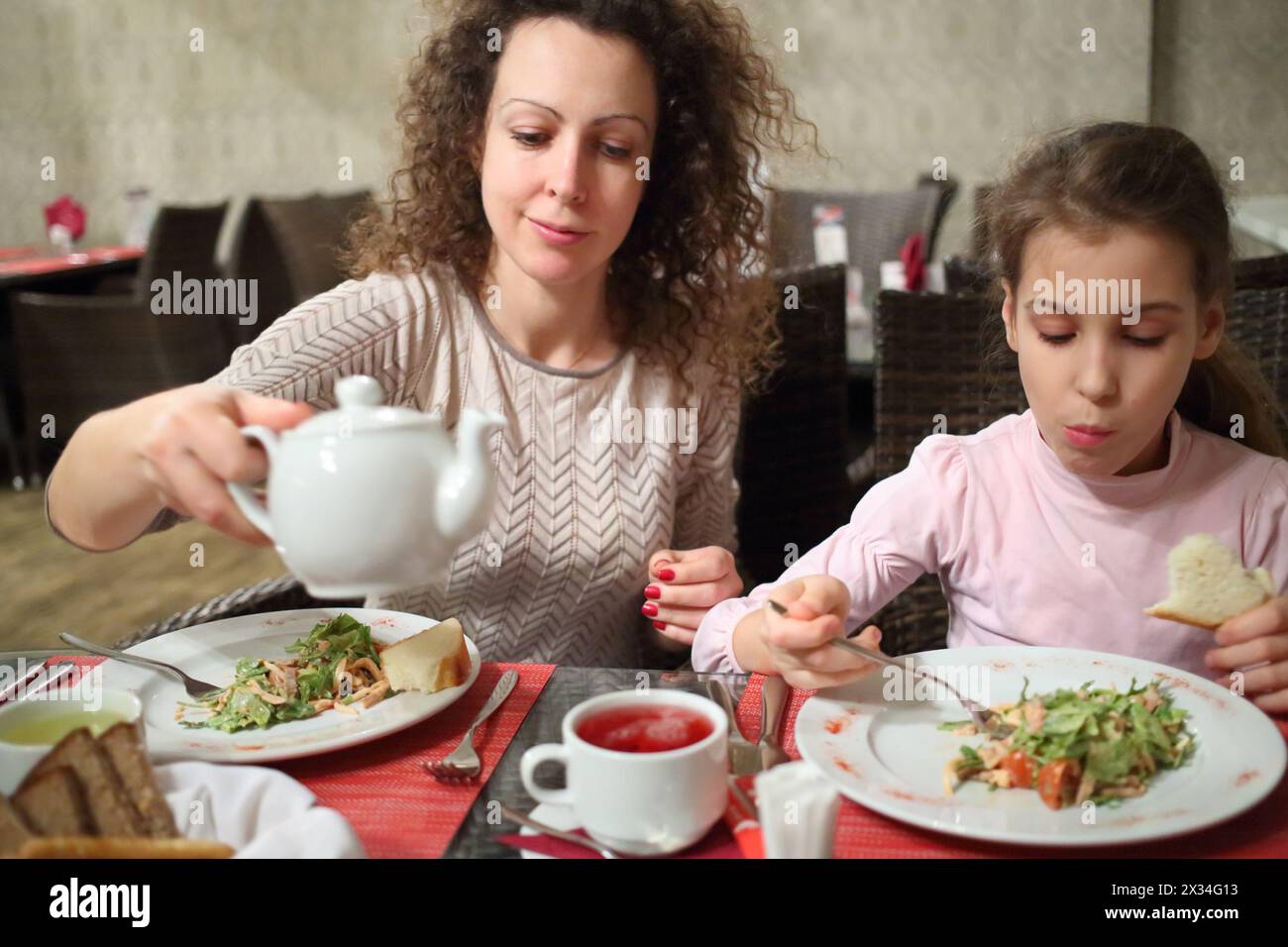 Mother and daughter eating salad and drinking tea at a table in a restaurant Stock Photo