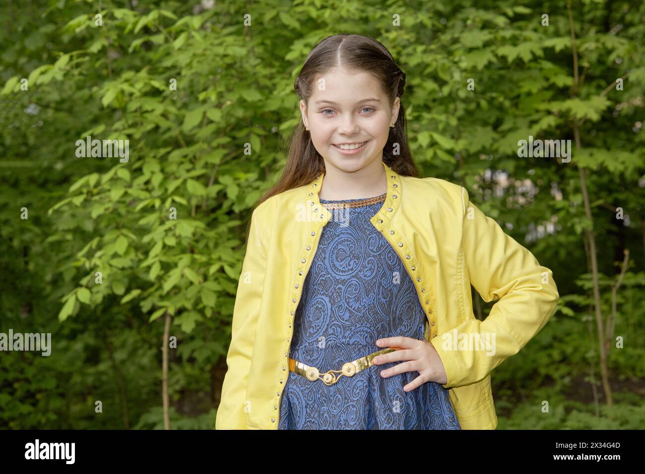 Half-length portrait of smiling girl in yellow jacket in green park. Stock Photo