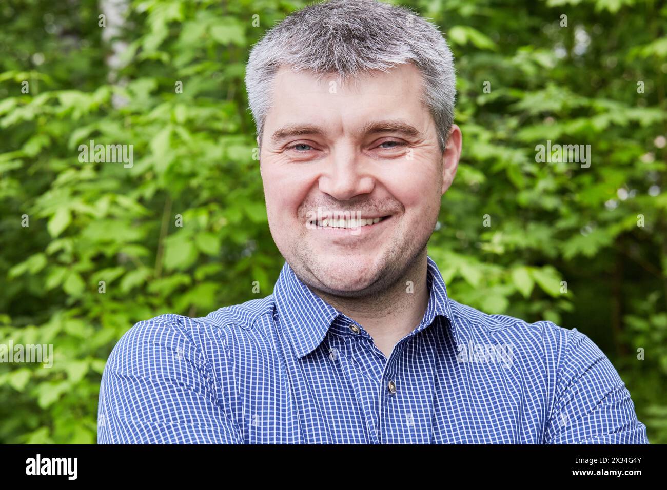 Humeral portrait of grey-haired smiling man in checkered shirt at summer park. Stock Photo