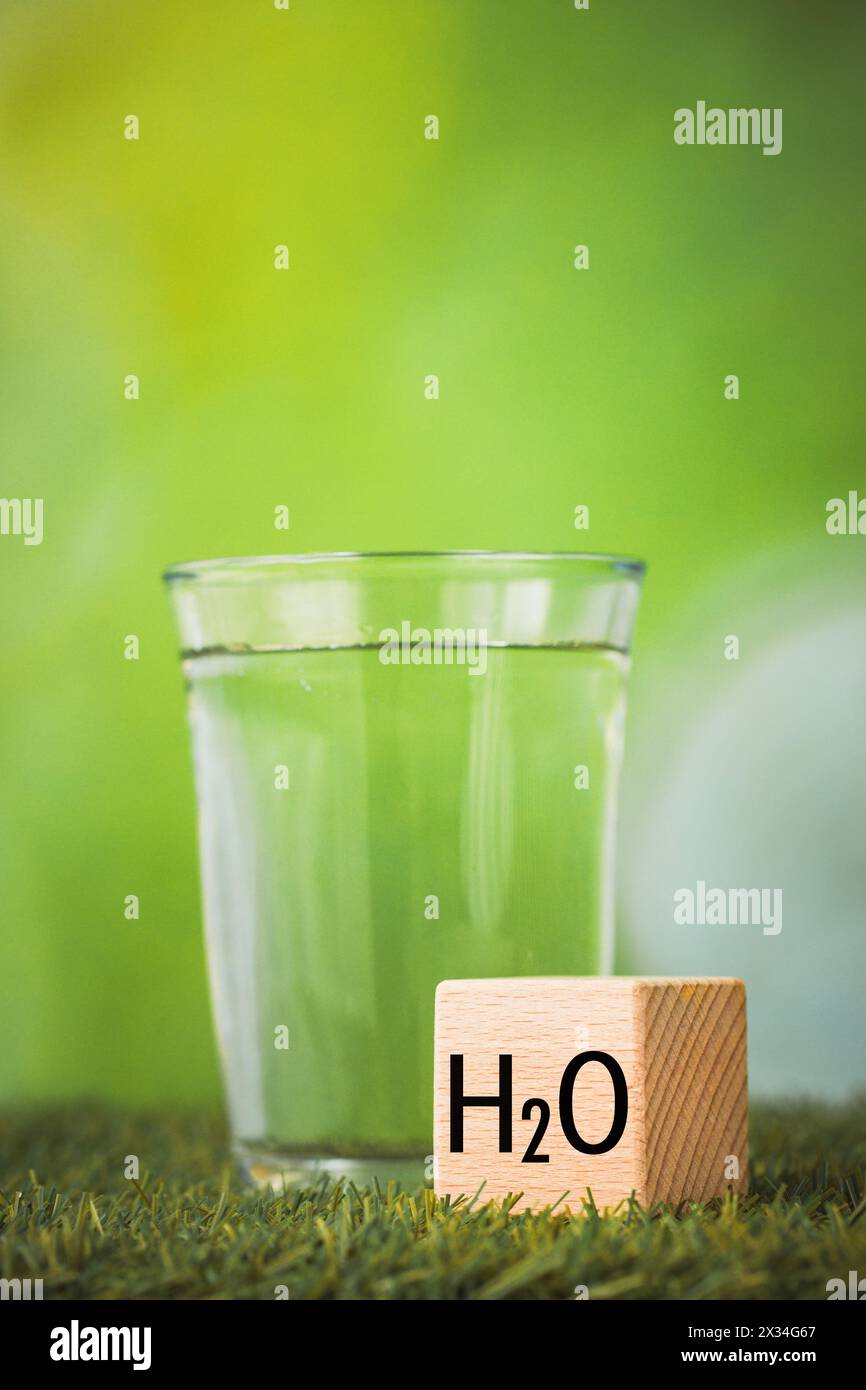 h2o water, Impact of water on the environment, Environmental science concept, Glass of water on green background, wooden block with h2o symbol, Vertic Stock Photo