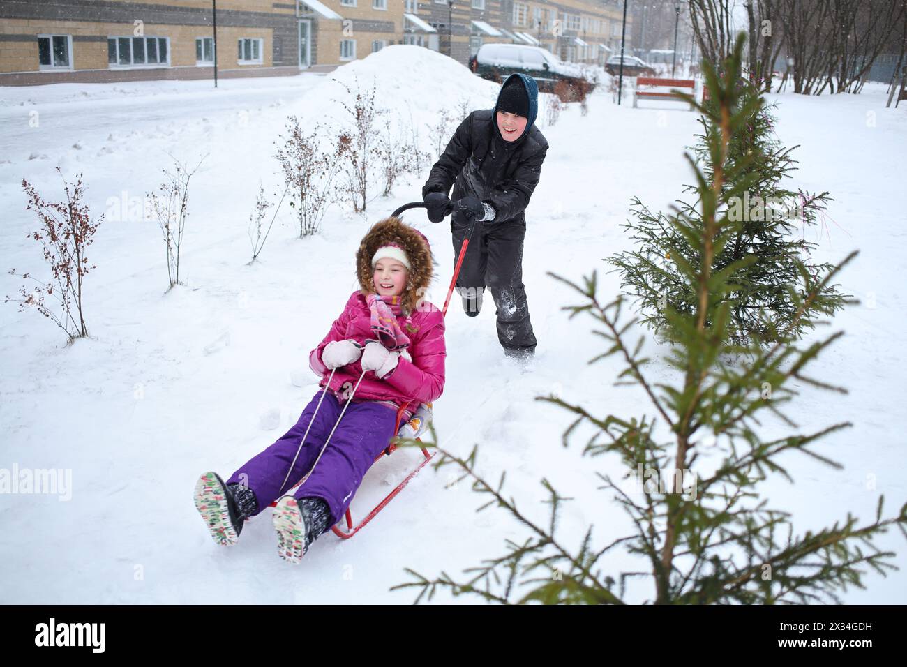 Happy boy rolling a girl on a sled near the apartment complex Stock Photo