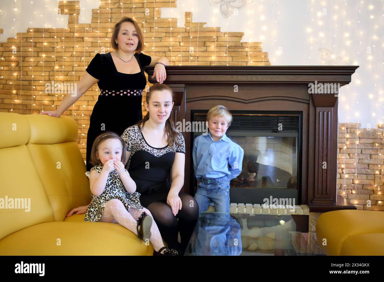 Family of four people in elegant clothes sit on a sofa near the fireplace Stock Photo