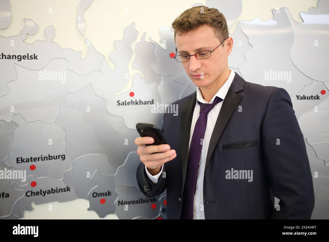 Portrait of businessman with phone leaning against wall with map Stock Photo