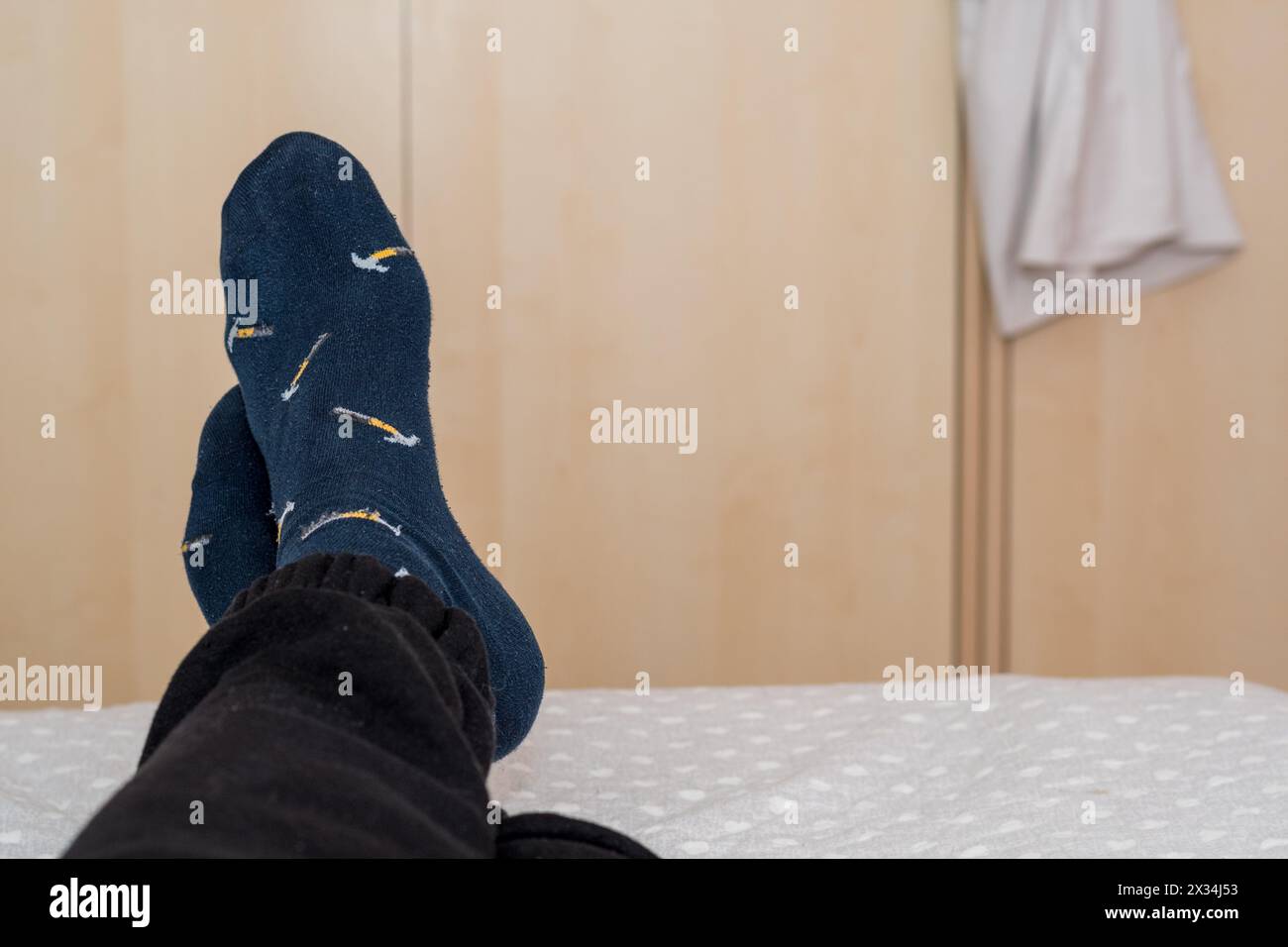 Man's feet crossed at the edge of the bed, relaxing in the room, nice blue socks. Stock Photo