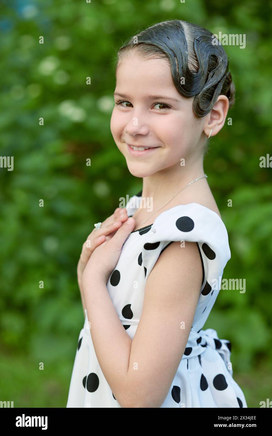 Half-length portrait of smiling little girl dressed in polka-dotted gown with hairdo. Stock Photo