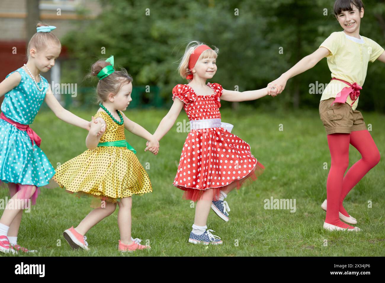 Four girls dance holding hands at grassy lawn. Stock Photo