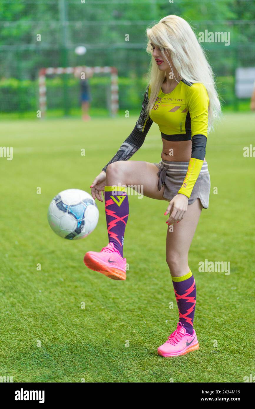 MOSCOW - JUL 16, 2015: Beautiful blonde woman (with model release) with long hair playing with ball on soccer field Stock Photo