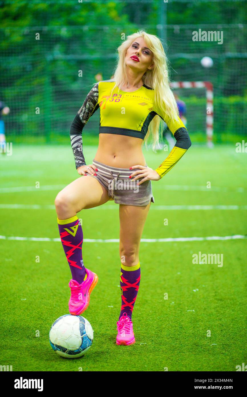 MOSCOW - JUL 16, 2015: beautiful blonde woman (with model release) in top with ball on soccer field, hands on waist Stock Photo