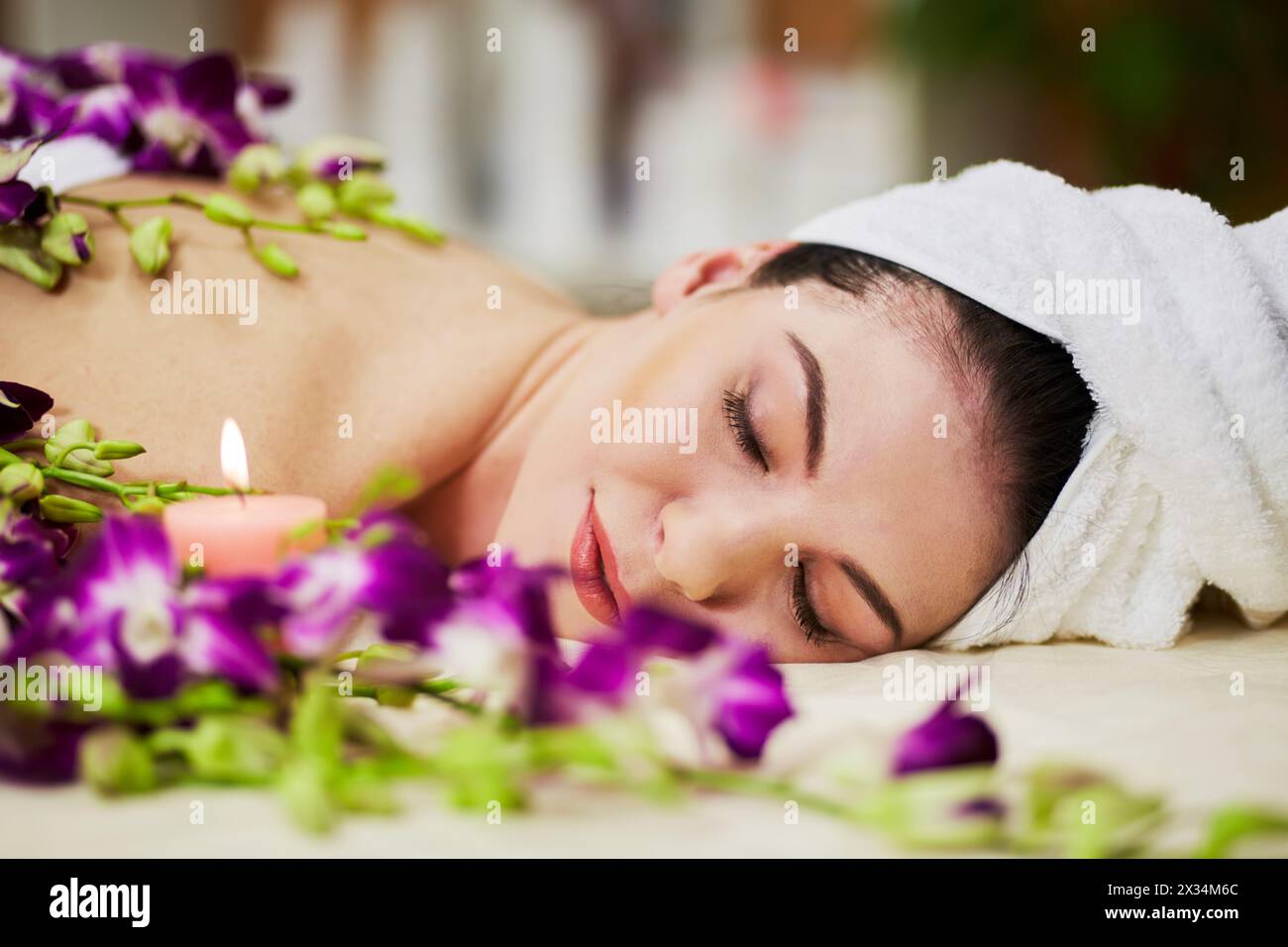 Face of woman that lies with her eyes close on couch among flowers and burning candle in beauty salon. Stock Photo