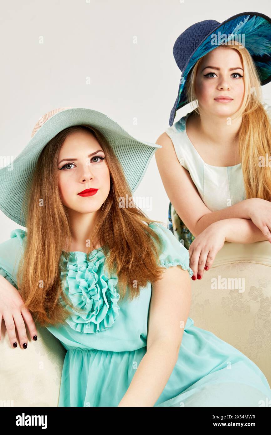 Two young blond women in wide-brimmed hats in studio. Stock Photo