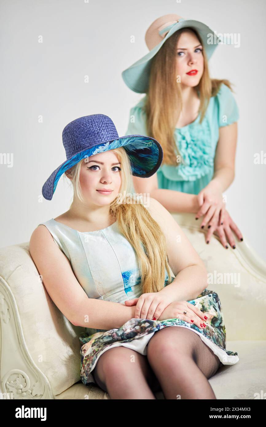 Two young blond women in wide-brimmed hats in studio, focus on first girl. Stock Photo