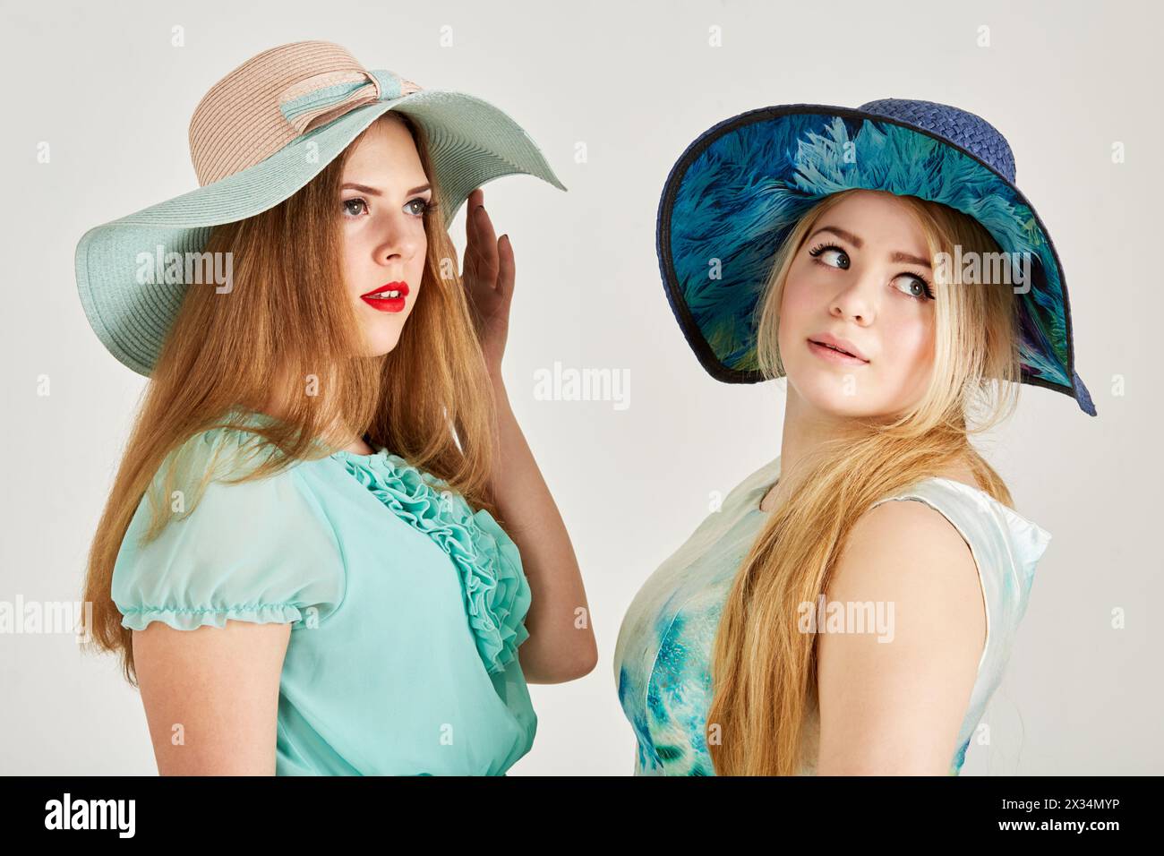 Two young blond women in wide-brimmed hats in studio. Stock Photo