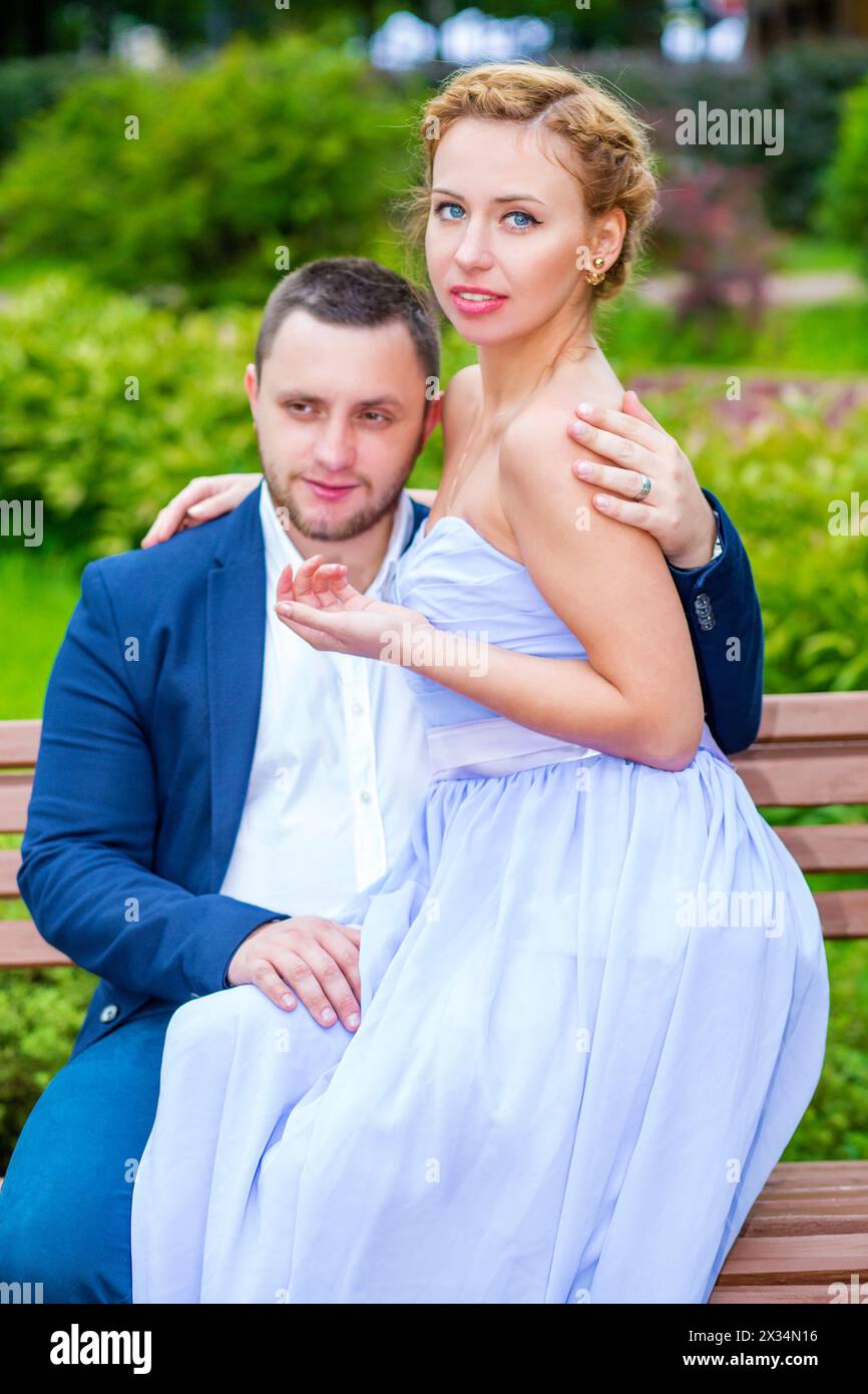 Man and woman embrace and sit on wooden bench in green summer park ...