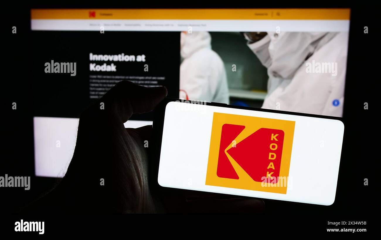 Person holding mobile phone with logo of American electronics business Eastman Kodak Company in front of web page. Focus on phone display. Stock Photo