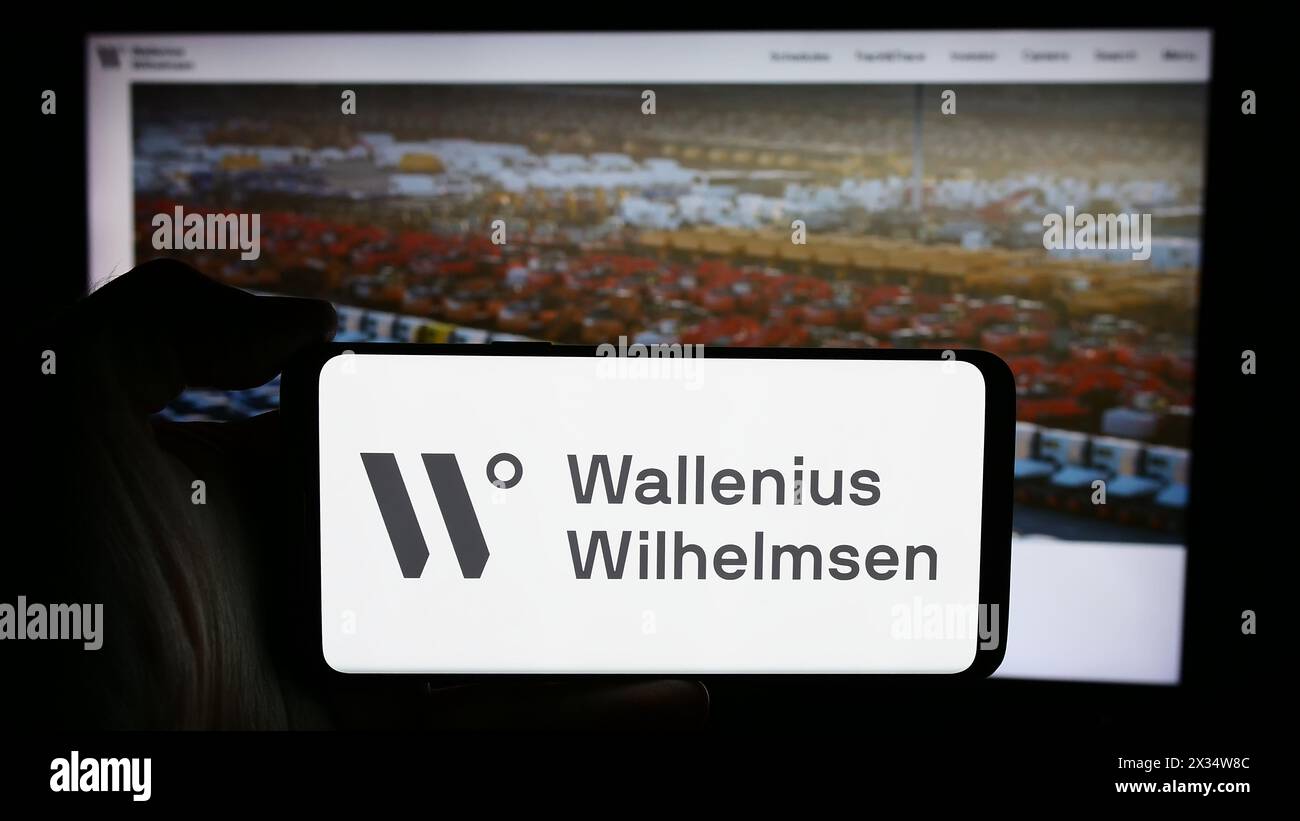 Person holding cellphone with logo of shipping company Wallenius Wilhelmsen ASA in front of business webpage. Focus on phone display. Stock Photo