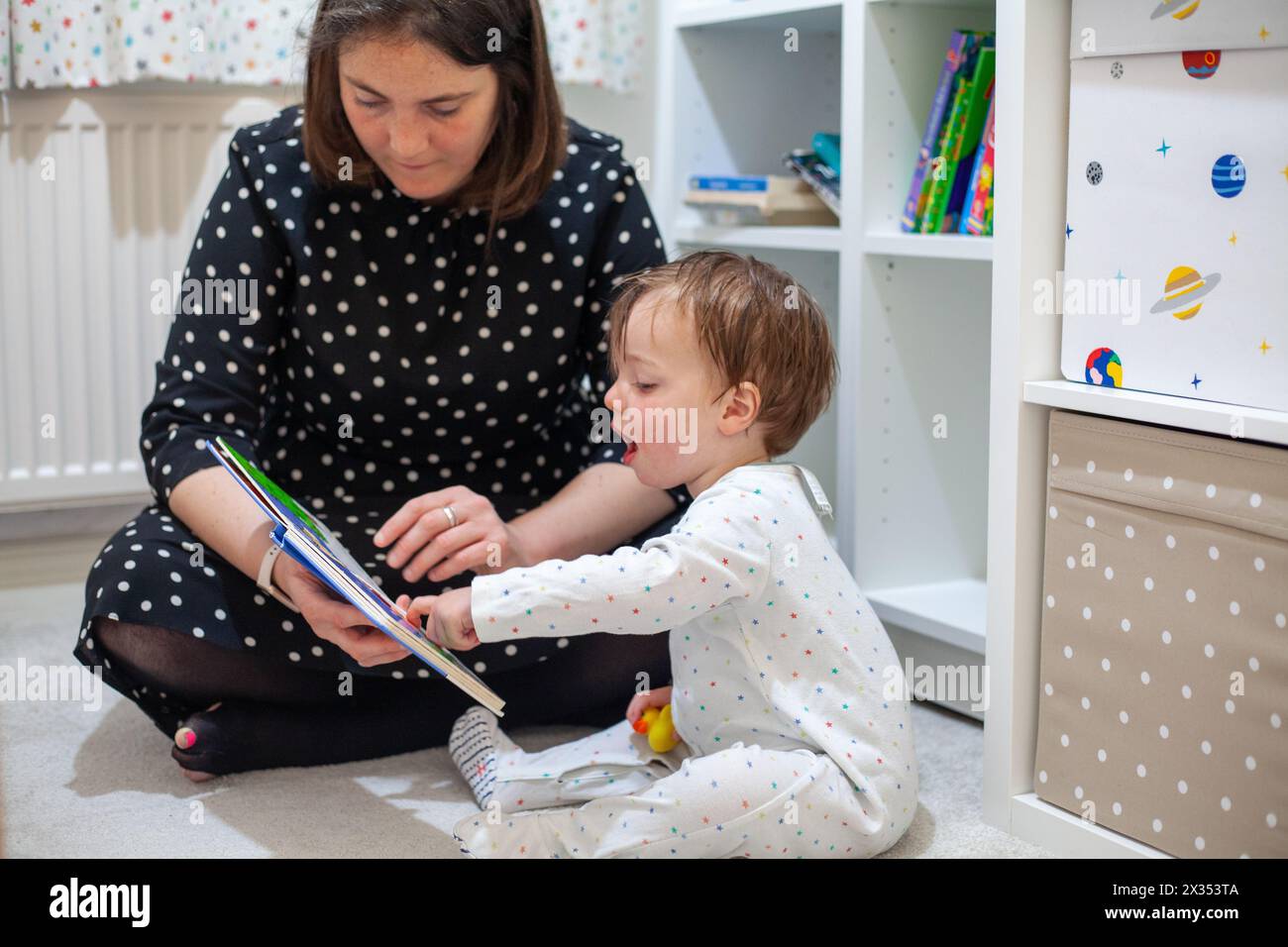 A heartwarming moment as a mother reads a bedtime story to her 2-year-old son. Stock Photo