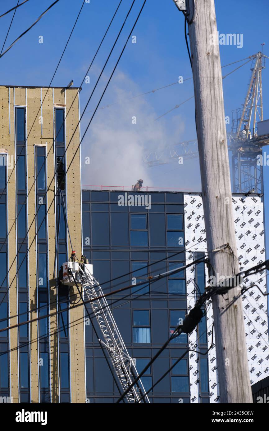 Halifax, Nova Scotia. April 23, 2024.   Firefighter inspecting to roof as they manage to control a Large fire of the roof of a new apartment building under construction, under watchful eyes of crew in ladder. Stock Photo