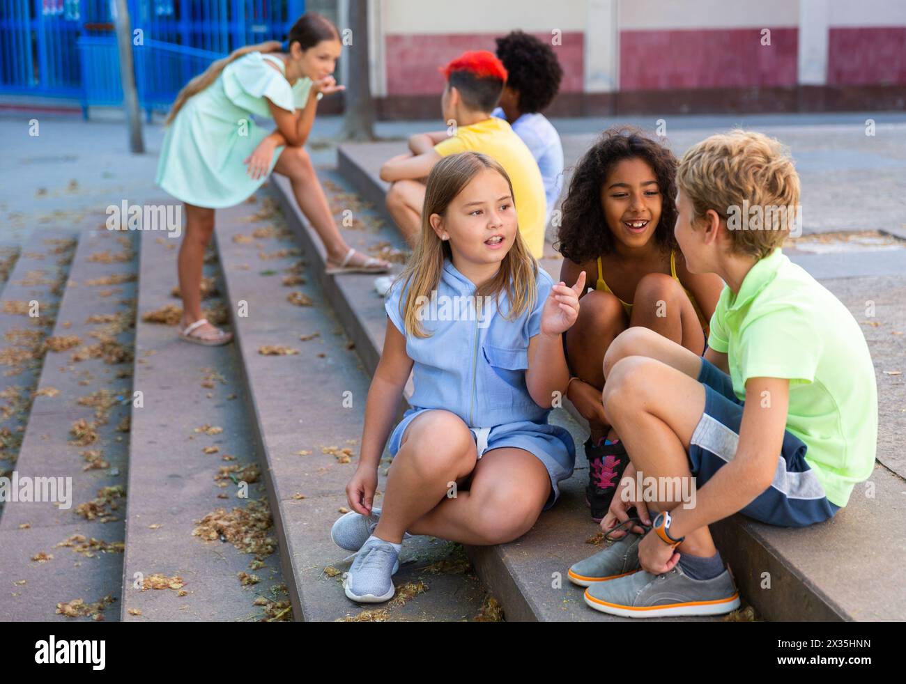 Positive tweenagers friendly blabbing while sitting on steps outdoors Stock Photo