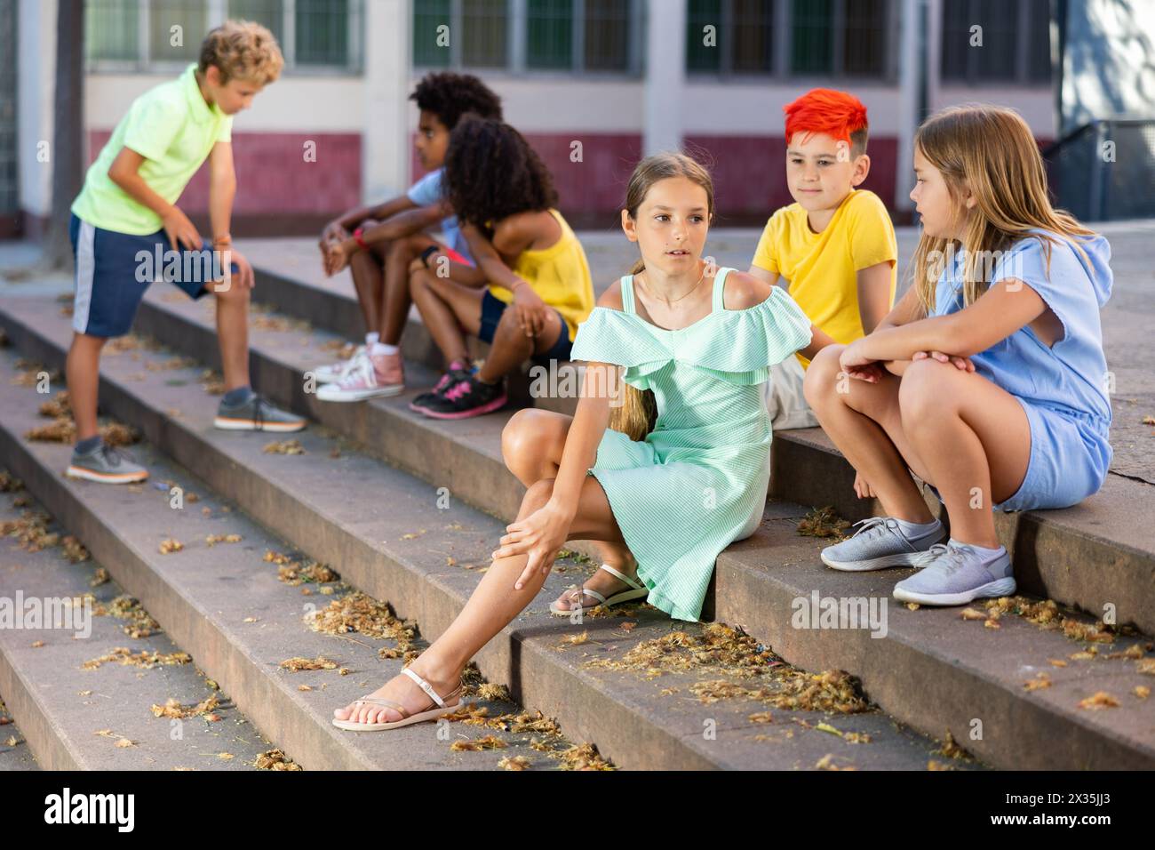 Positive tweenagers friendly blabbing while sitting on steps outdoors Stock Photo
