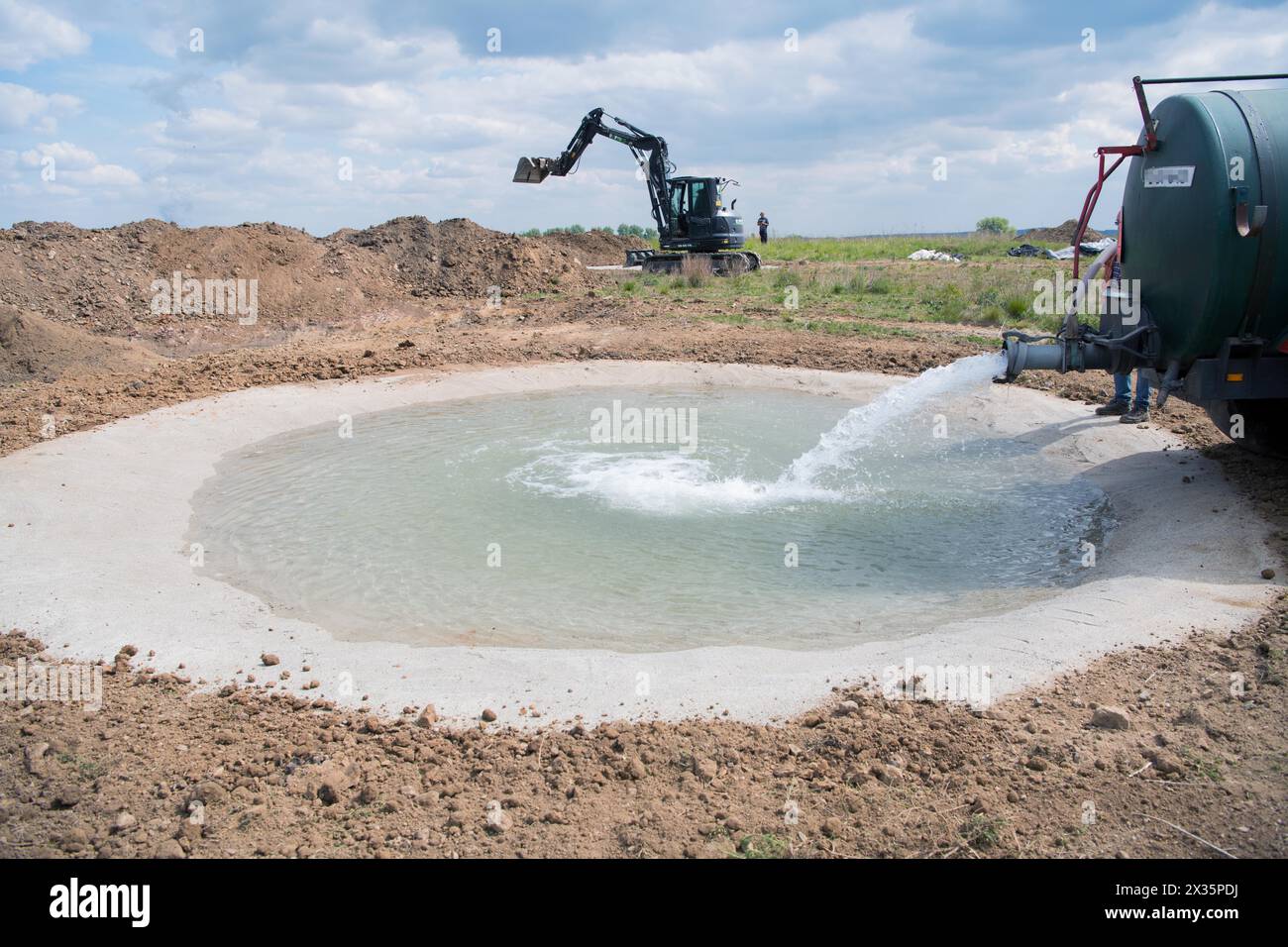 Species protection, tractor with water tank fills newly created spawning waters for amphibians in cultivated landscape, Stolberg, North Stock Photo