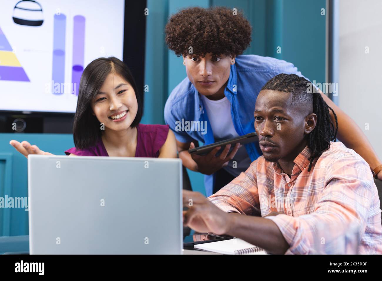 Diverse group of young colleagues focusing on laptop screen in a modern business office Stock Photo