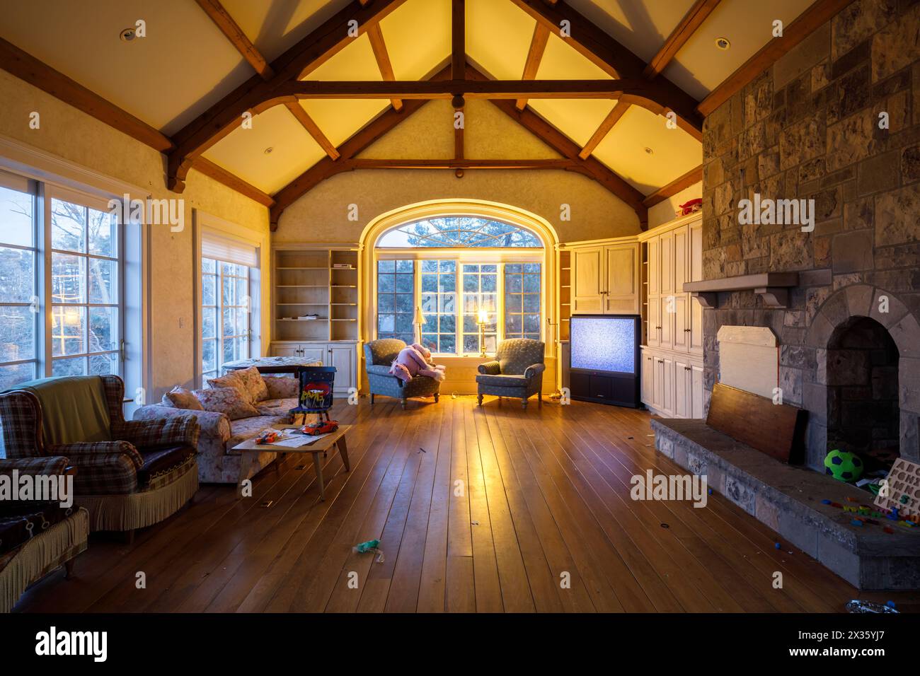 A living room with a cathedral ceiling and wooden joists and illuminated at dusk, inside an abandoned house. This House has since been demolished. Stock Photo