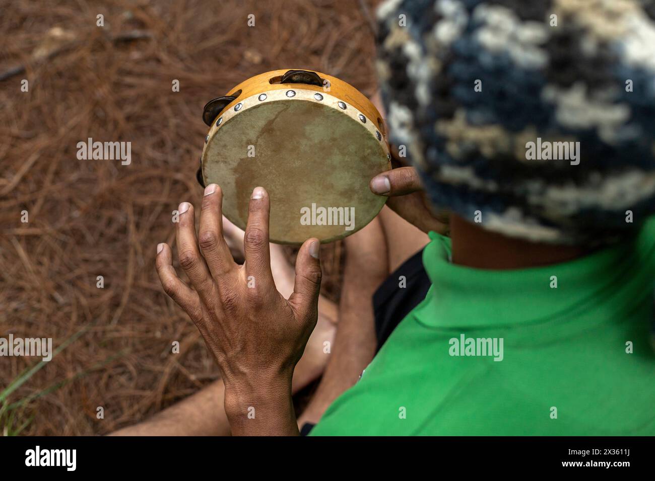 Top view of an unrecognizable Latin American man playing a tambourine, he is barefoot in a pine forest. Concept yoga class and music. Stock Photo