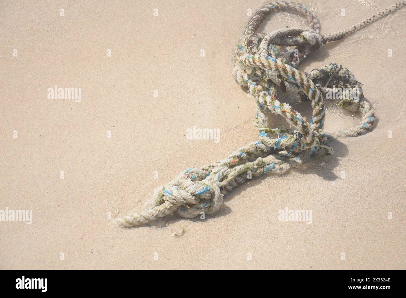 A rope is laying on the sand. The rope is white and blue Stock Photo