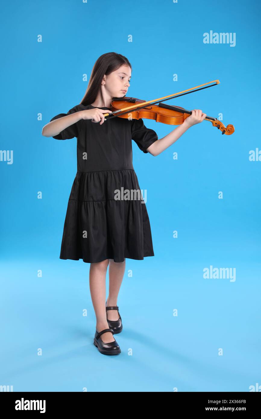 Preteen girl playing violin on light blue background Stock Photo