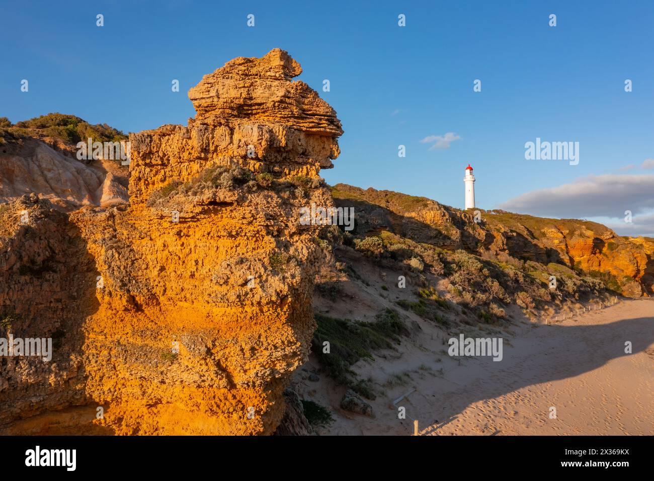 Distant view of a white lighthouse on eroded cliff tops above a rugged coastline at Aireys Inlet on the Great Ocean Road in Victoria, Australia Stock Photo