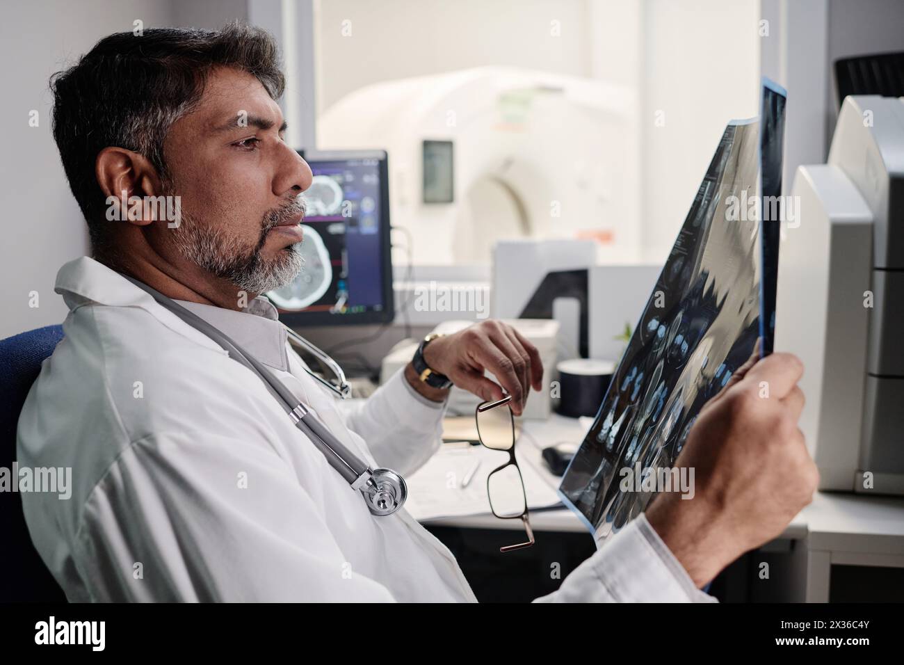 Side view of biracial male radiographer sitting at table in office ...