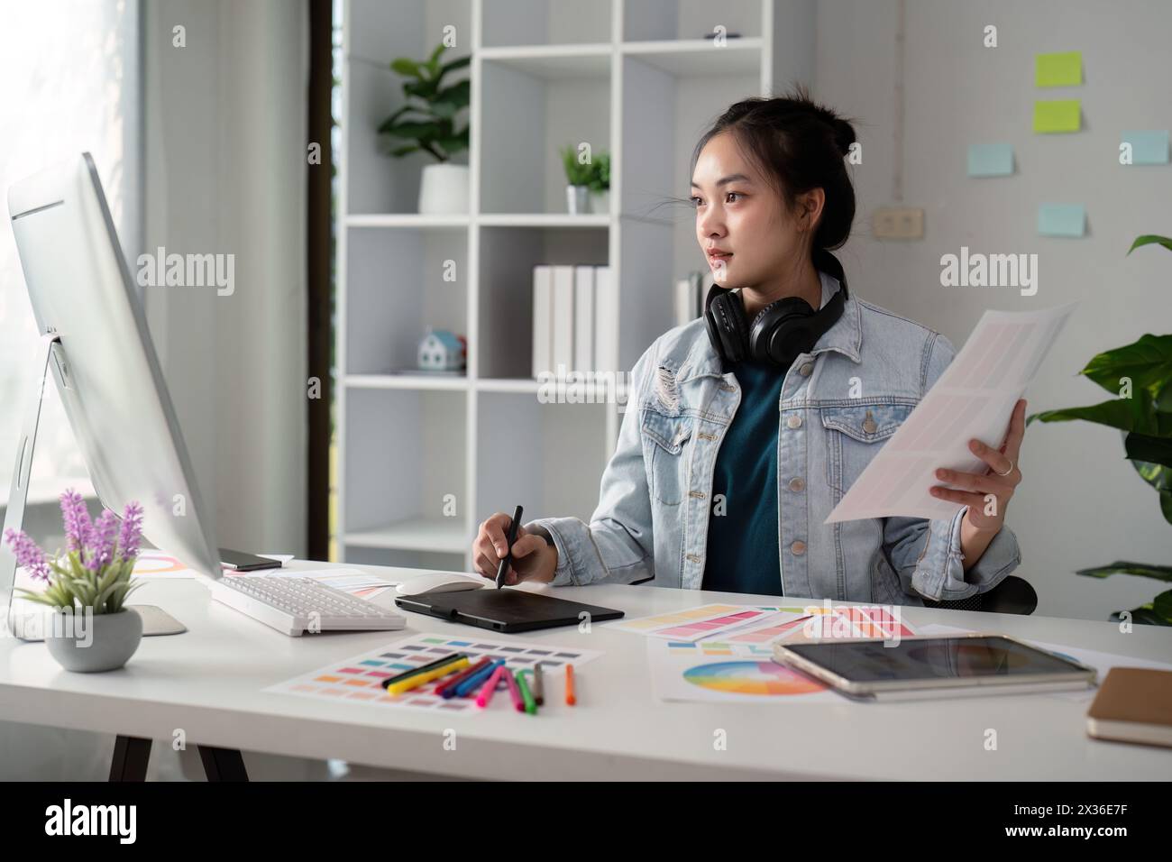 Asian woman freelance graphic designer working with color swatch samples and computer at desk in home office, young lady choosing color gamma for new Stock Photo