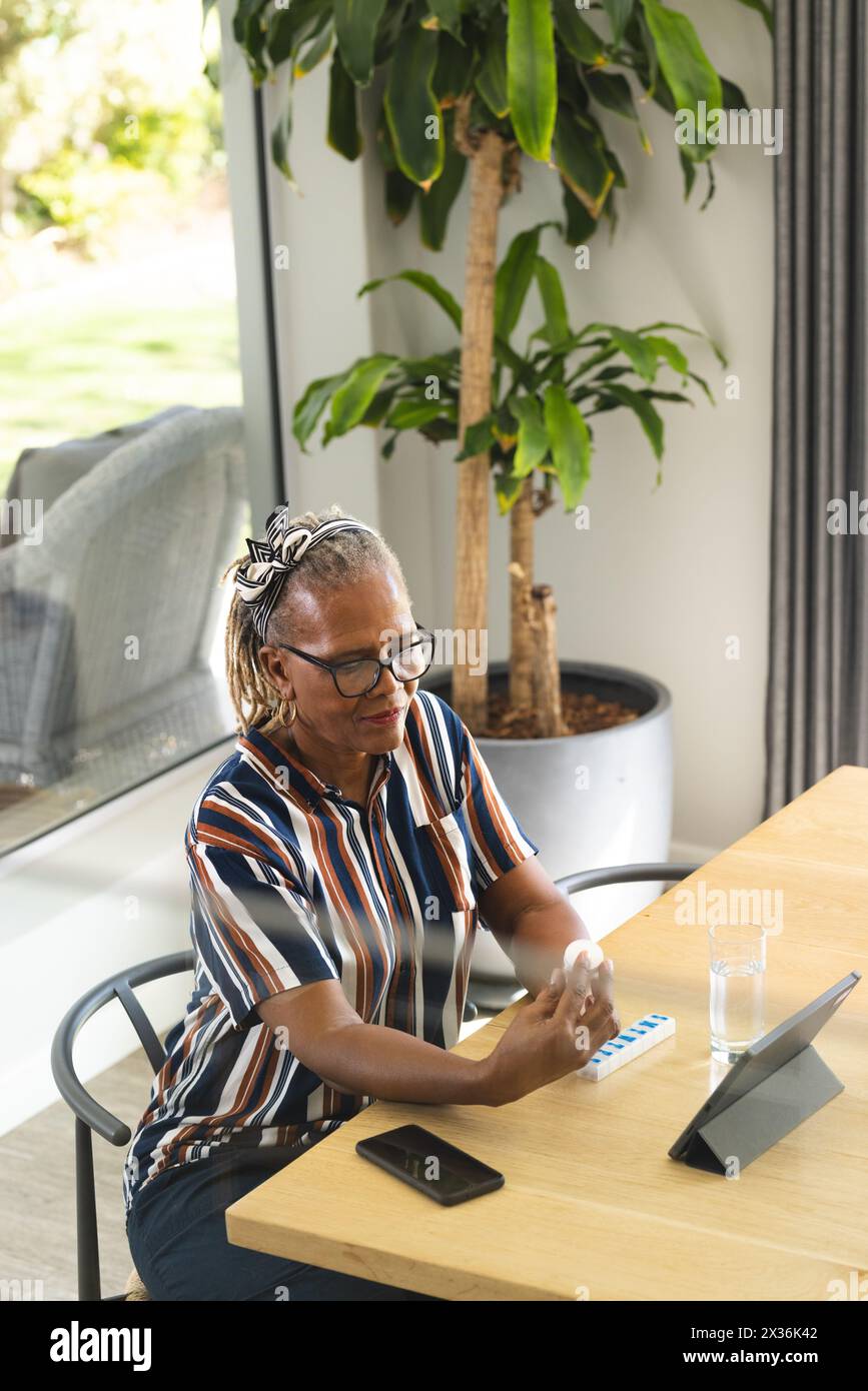 African American senior woman at home using smartphone, tablet, taking medicine Stock Photo
