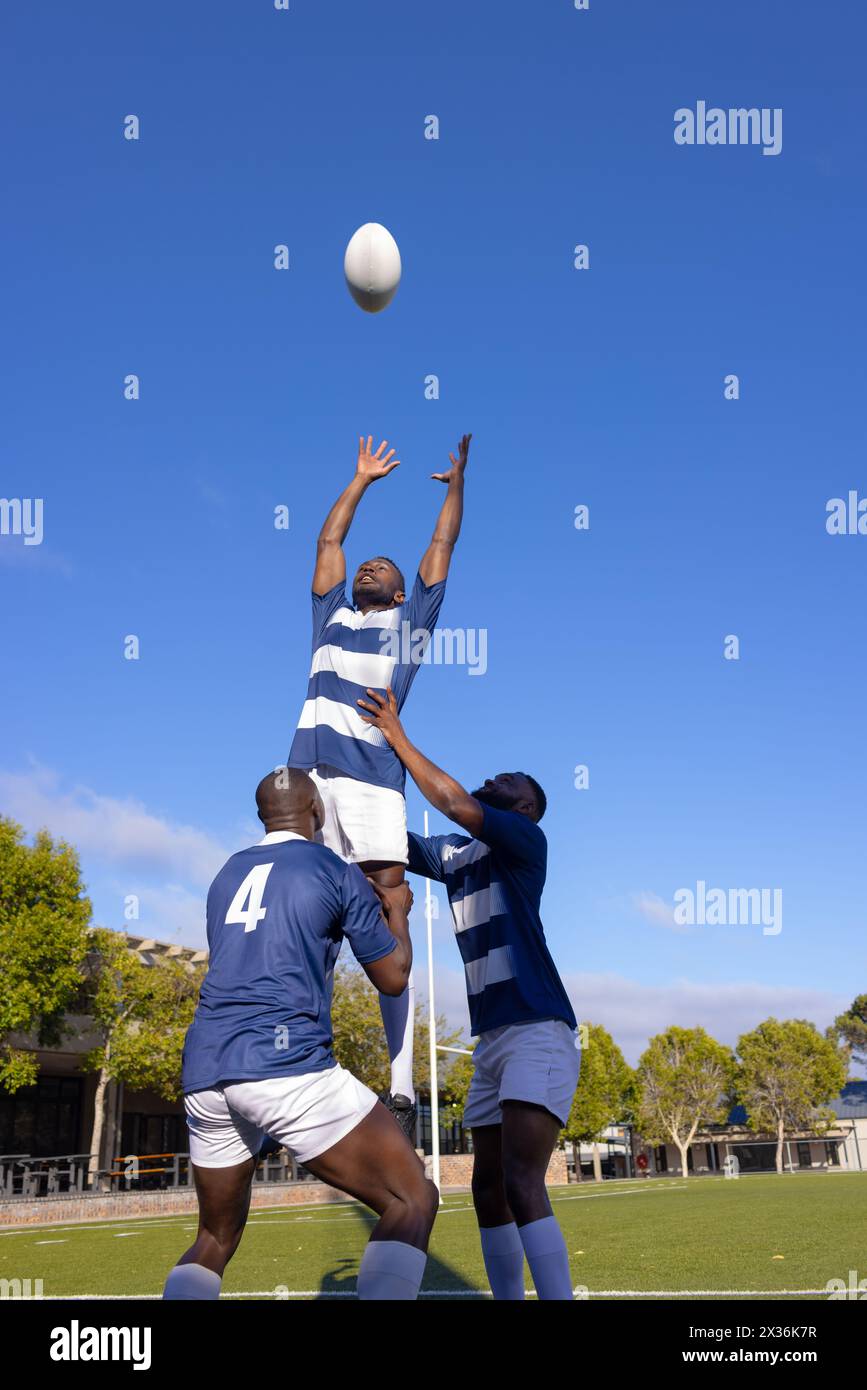 Three young African American men play rugby, one leaps for the ball Stock Photo