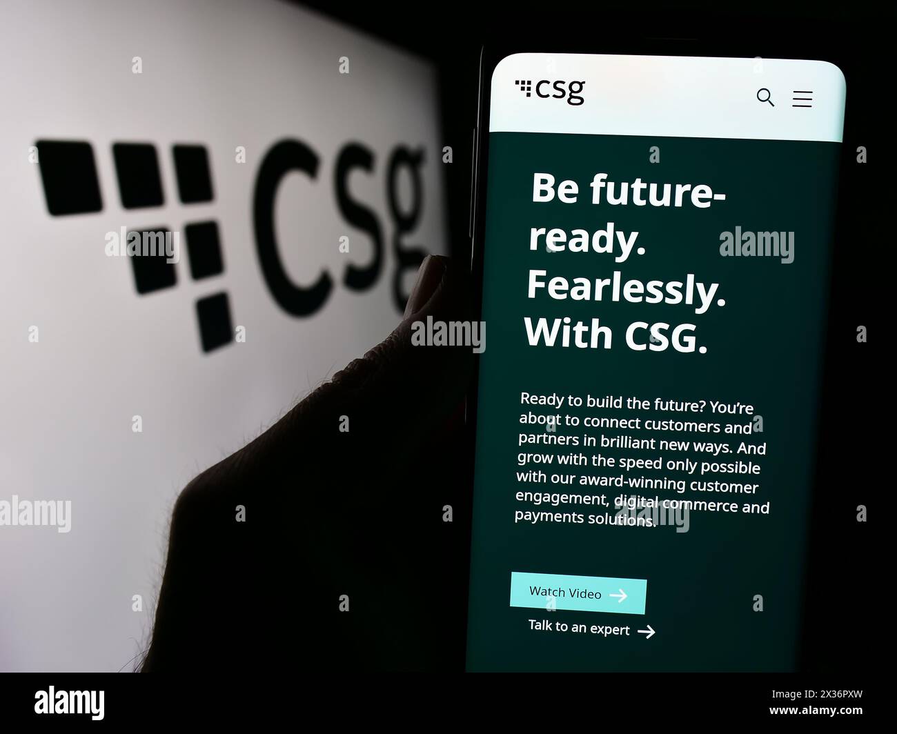 Person holding smartphone with webpage of US BSS software company CSG Systems Inc. in front of business logo. Focus on center of phone display. Stock Photo