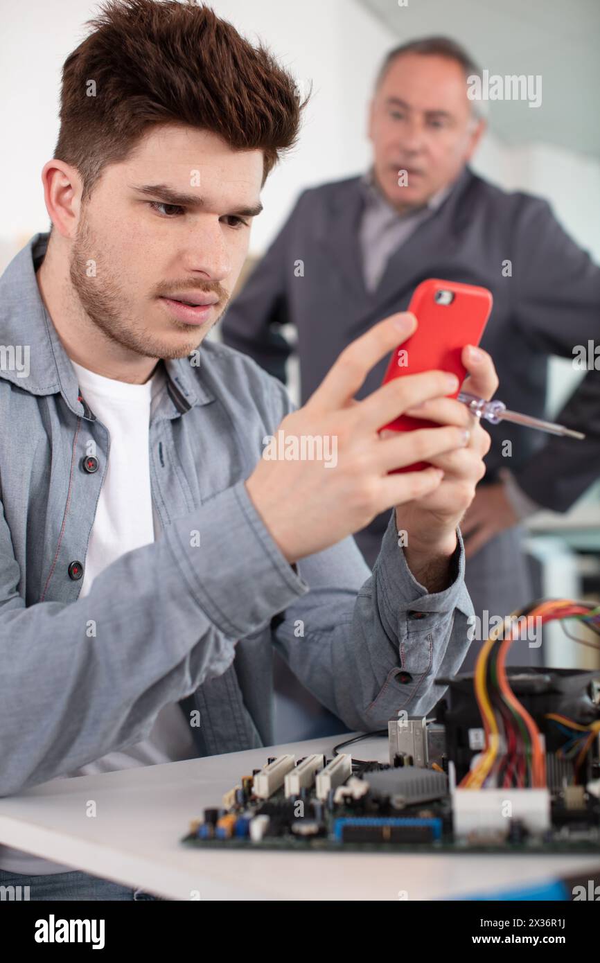 angry teacher behind electrician apprentice looking at his smartphone Stock Photo