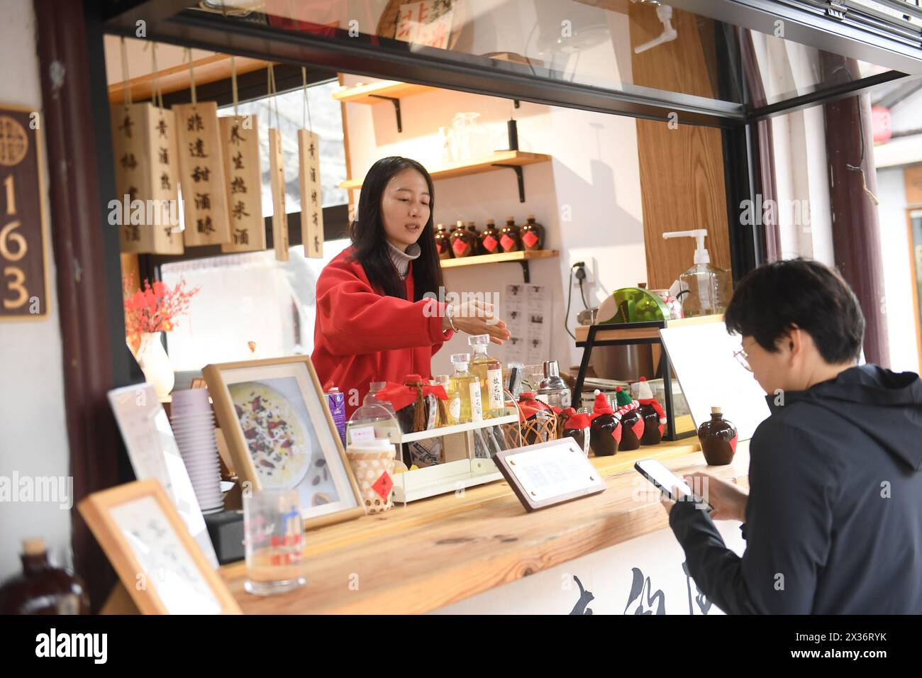 (240425) -- SHAOXING, April 25, 2024 (Xinhua) -- A clerk guides a customer to pay via her mobile phone for specialty coffee flavored with yellow rice wine at a store in Cangqiao Straight Street in Shaoxing, east China's Zhejiang Province, Feb. 20, 2024. Cangqiao Zhijie, literally translated as 'Cangqiao Straight Street,' is a historical and cultural site featuring ancient houses of unique style. Covering an area of 0.064 square kilometers, the 1,500 meters long street could be traced back to the Song Dynasty (960-1279). Restoration and protection efforts have been ongoing here since the 1990s. Stock Photo