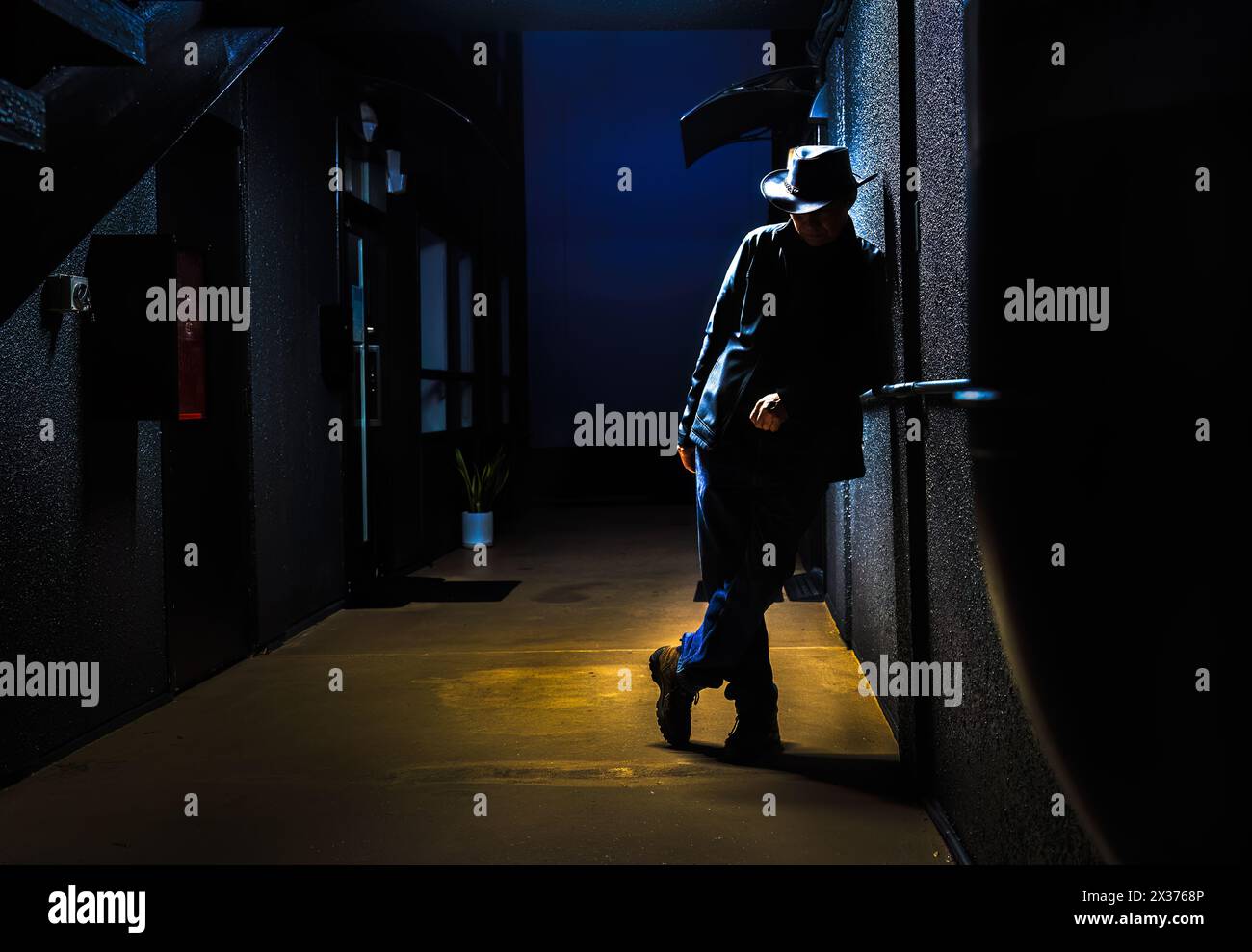 Silhouette of a man leaning against a wall in a dark alleyway at night. Depression and loneliness concept. Stock Photo
