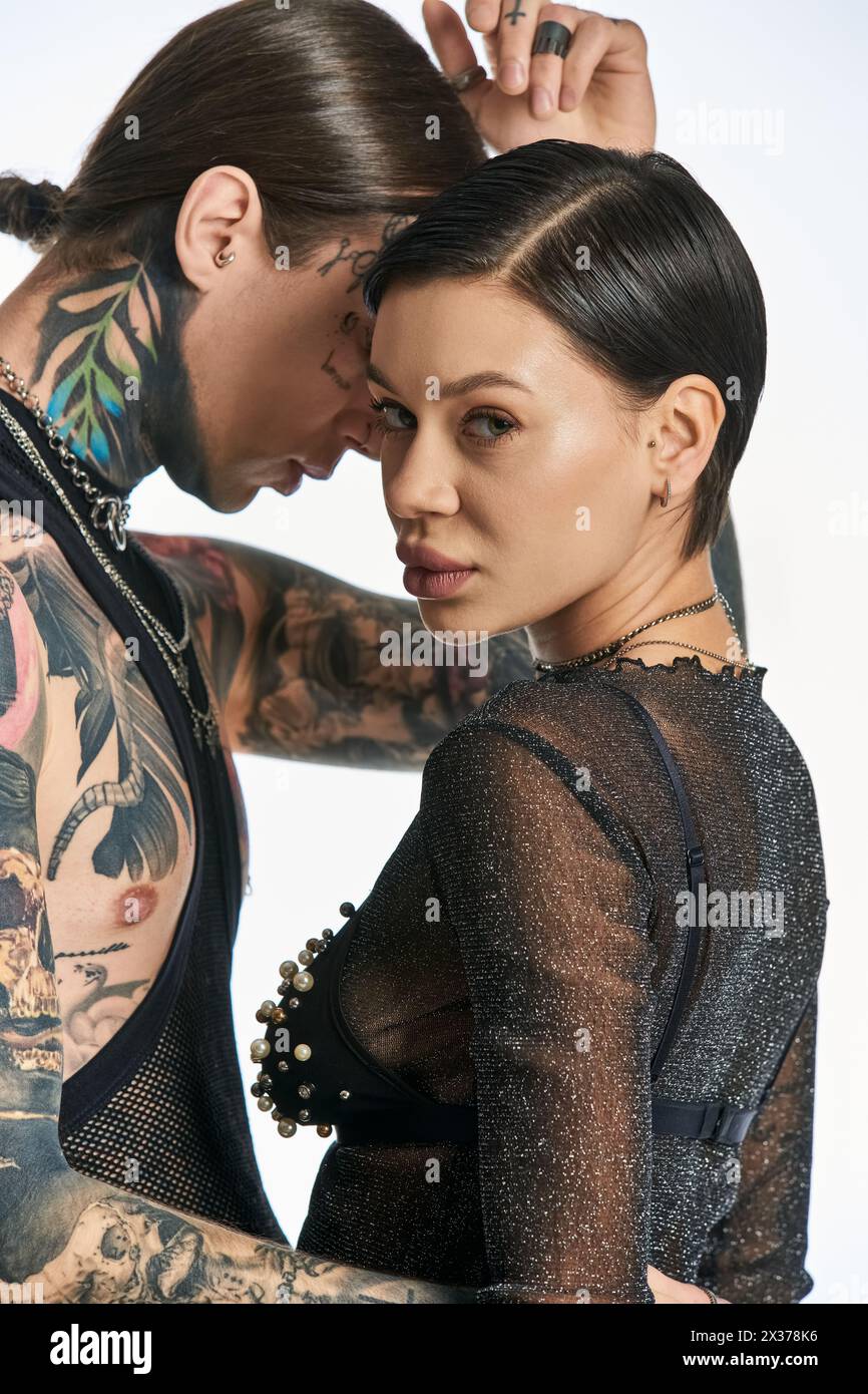 A stylish young man and woman with intricate arm tattoos posing in a studio against a grey background. Stock Photo