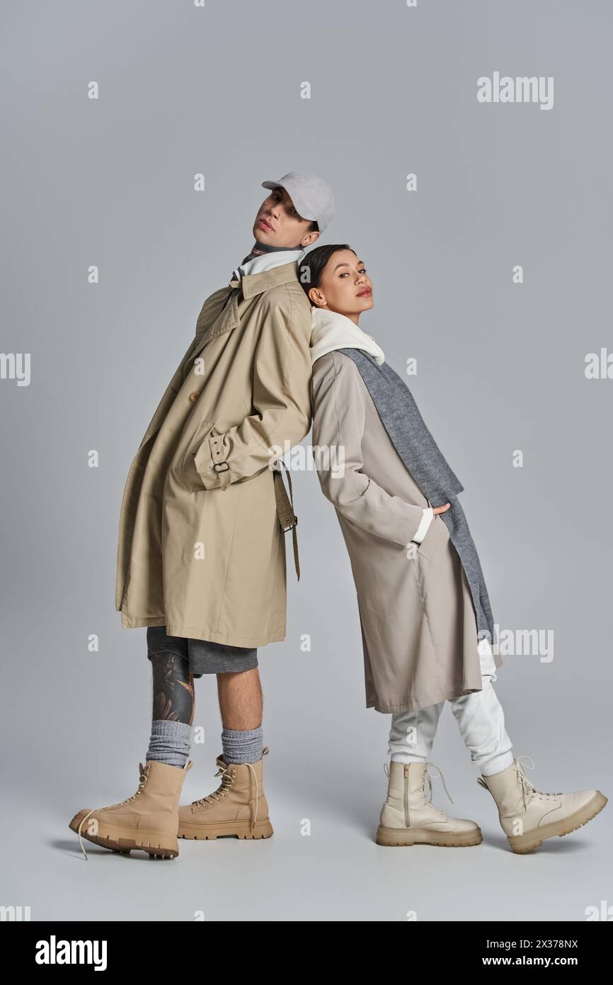 A stylish young man in a trench coat and hat standing next to another ...